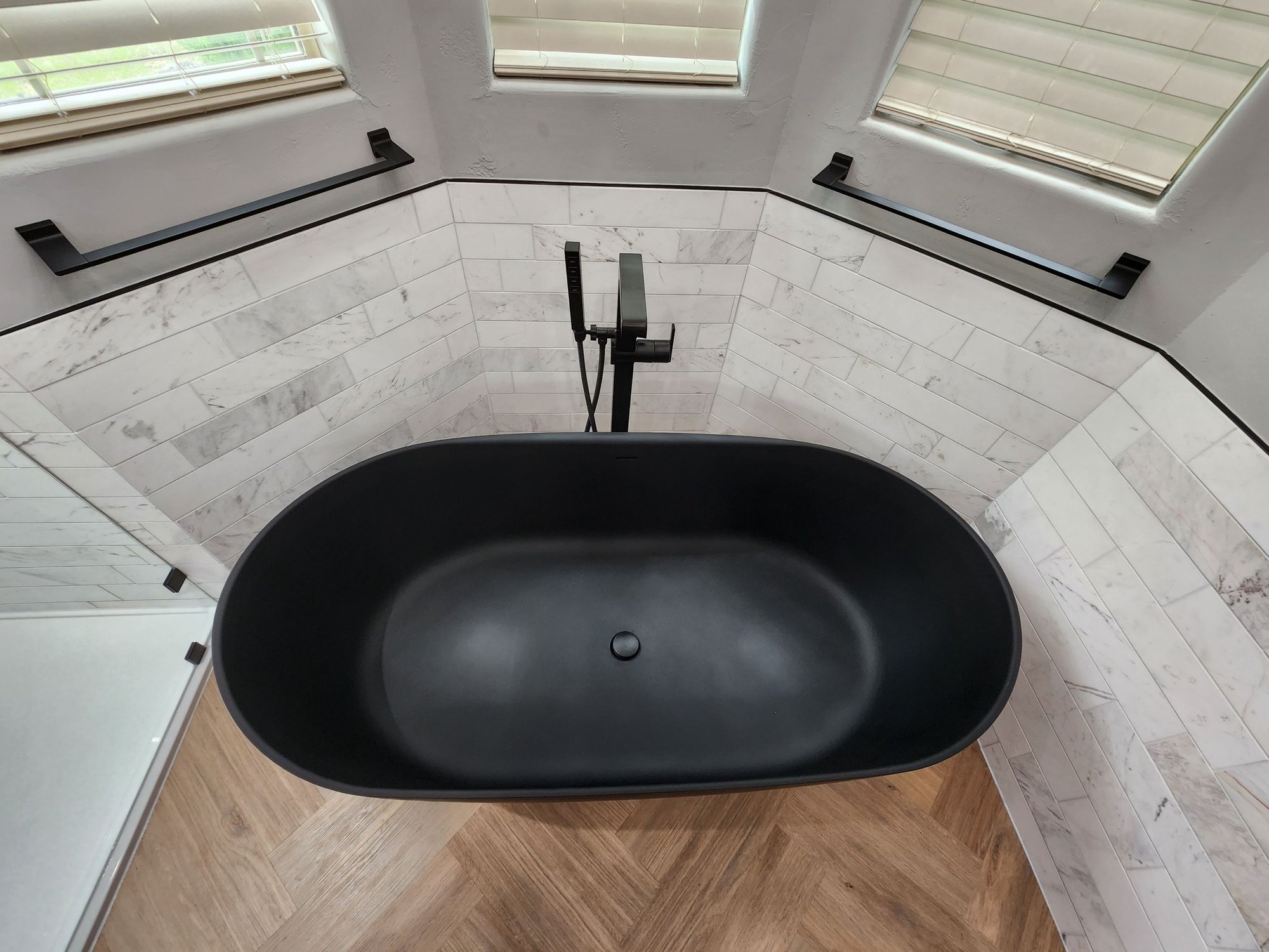 modern black tub in a san antonio bathroom remodel with marble tile and chevron wood floors